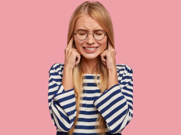 Une femme blonde à lunettes rondes qui se bouche les oreilles parce qu''il y a trop de bruit